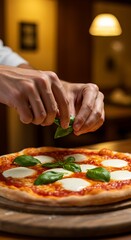Italian-style Margherita pizza being garnished with fresh basil by hand, kitchen background blurred