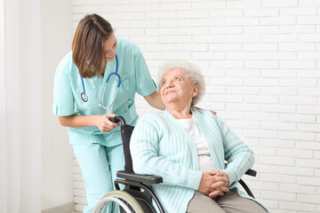 Obraz premium Young nurse with senior woman in wheelchair near white brick wall