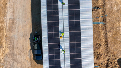 Two workers in safety gear installing solar panels on a rooftop, highlighting renewable energy,...