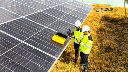 Two workers in safety gear inspecting solar panels in a field, emphasizing renewable energy,...