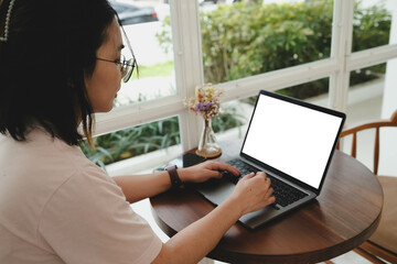 Person using laptop with blank screen at round wooden table near window in cozy cafe, ideal for showcasing software, mockup, dashboard, or online workspace concept.