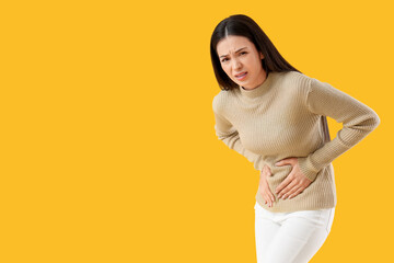 Young woman suffering from bellyache on yellow background