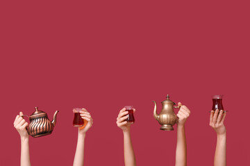 Female hands with Turkish tea and teapots on red background
