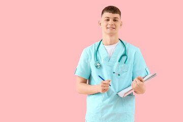Male medical intern with notebook on pink background