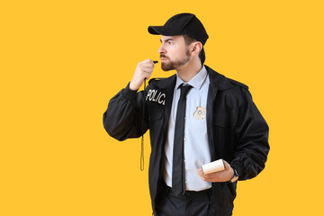 Male police officer with notebook and whistle on yellow background