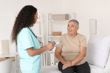 Obraz premium Young African-American nurse working with senior woman in hospital room