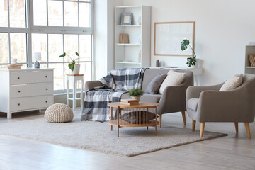 Interior of light living room with grey sofa, armchair and table