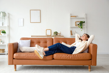 Beautiful young woman lying on brown couch at home