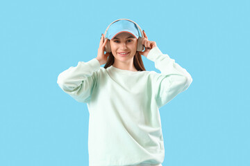 Stylish young woman in cap on blue background