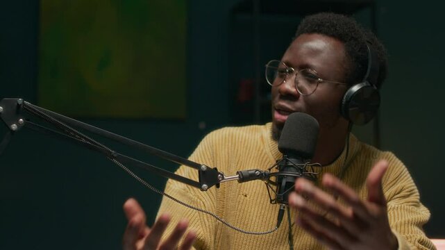Handheld shot of young African American host talking to adult Caucasian male influencer in microphone during podcast recording in studio