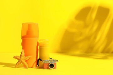 Bottles of sunscreen, mini photo camera, starfish and palm leaf shadow on yellow background