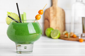 Glass of green bloody mary cocktail garnished with physalis berries and lime on white wooden...