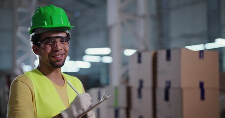 Smiling female industrial worker wearing safety equipment standing in blurred warehouse taking notes - Powered by Adobe