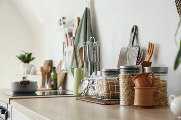 Jars of pasta with utensils on counter near light wall in kitchen, closeup