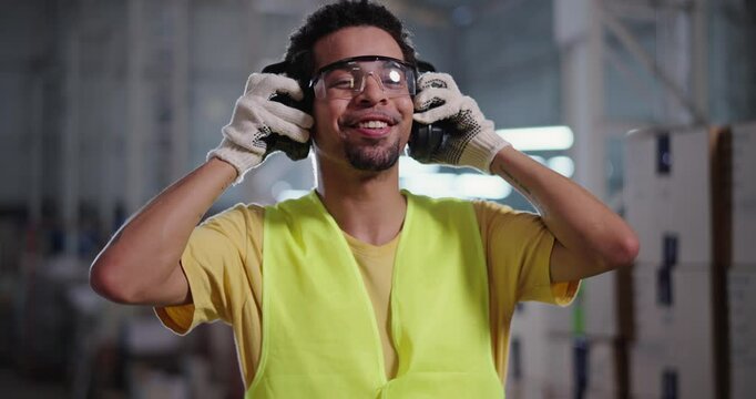 Young worker standing in warehouse putting on ear plugs and smiling at camera.