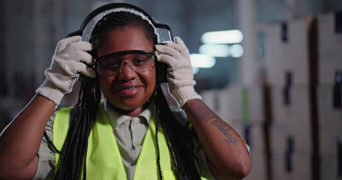 Female worker standing in warehouse putting on ear plugs and smiling at camera.