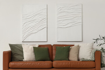 Brown leather sofa with soft pillows near white wall in living room