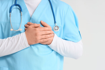 Male doctor keeping his hands on heart against light background, closeup