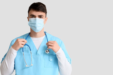 Male doctor in medical mask with stethoscope on light background