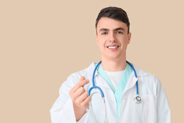 Male doctor making heart gesture on beige background, closeup