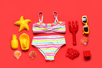 Composition with children swimsuit, sunglasses and beach sand molds on red background