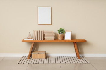 Photo frame, houseplant and books on bench near beige wall in interior of room