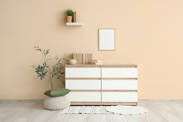Wicker box and books on chest of drawers near beige wall in interior of room