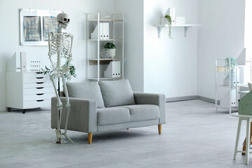 Interior of light hospital with human skeleton model and grey sofa