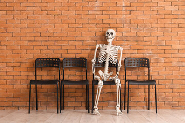Human skeleton model sitting in chair near brick wall