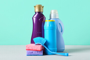 Set of cleaning supplies and bottles of detergent on turquoise background, closeup