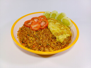Plate of Nasi Goreng (Indonesian fried rice), topped with a fried egg, fresh slices of red tomatoes, and green cucumbers. Presented on a yellow-rimmed plate against a clean, plain white background