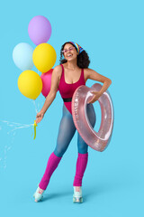 Young African-American woman in roller skates with swim ring and balloons on blue background. Summer party