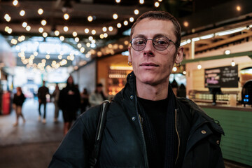 Obraz premium Stylish man wearing glasses posing in a modern food market with people walking