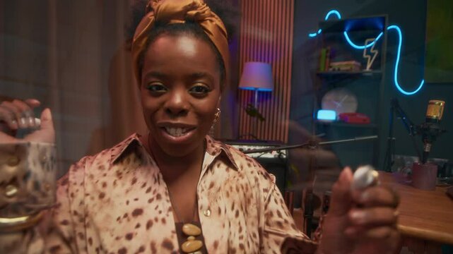 Handheld zoom in shot of cheerful female African American musician in elegant clothes autographing camera lens when giving interview in podcast studio