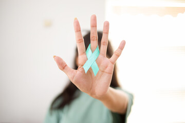 Close Up View of Female Hand Holding Turquoise Ribbon. Ovarian Cancer and Gynecological Disorders Concept.