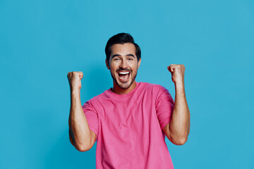 Full body excited happy cheerful young man wearing pink t-shirt celebrating success with raised...
