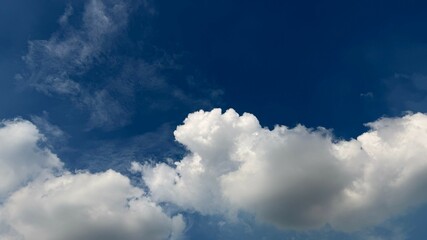 Puffy cumulus clouds are drifting through the clear blue sky during a sunny day