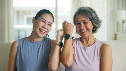 Adult child smile look at camera showing gift AI smart watch IOT app with middle age old mum. Love health care older mom asia elder people sit at home happy wear wrist trace help protect aging life. © ChayTee