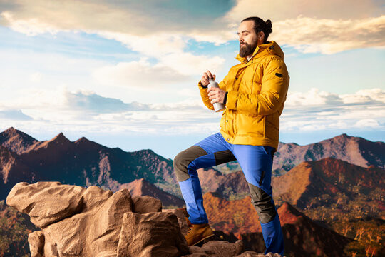 Young man explorer climbing the mountain range and hydrating with his water bottle, drinking refreshment on top of the rocky mountain. Male hiker refreshing after the trekking activity. - Powered by Adobe