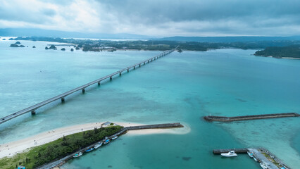 Obraz premium A Long bridge of Kouri Island and beach from a high view by drone with clear sky and sea water.