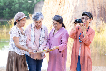 4 elderly women gathered together on scenic outdoor travel adventure, examining map and sharing location, Group entrepreneur elderly meeting hiking walking exercising together on holiday vacation.
