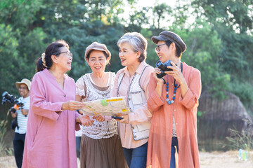 4 elderly women gathered together on scenic outdoor travel adventure, examining map and sharing location, Group entrepreneur elderly meeting hiking walking exercising together on holiday vacation.