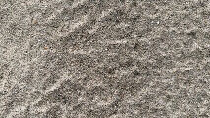 A closeup reveals intricate patterns and textures within a layer of gray sand on a beach
