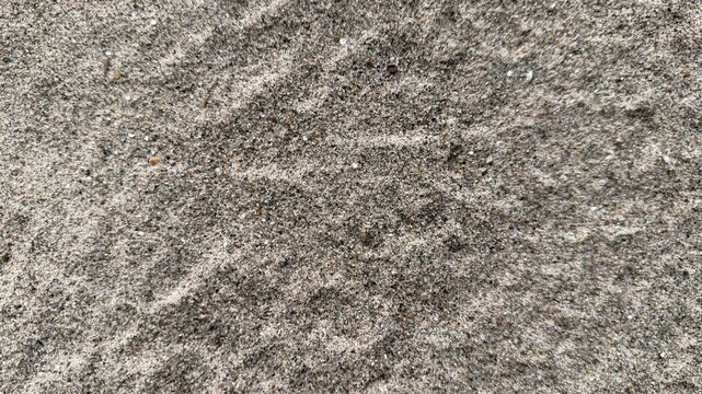 A closeup reveals intricate patterns and textures within a layer of gray sand on a beach
