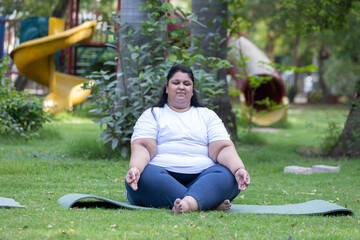 Indian woman do yoga meditation at summer park to loose weight and stress management. Plus size or fat man obesity problem. Mental health and fitness lifestyle. Balance life.