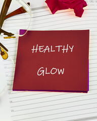 A note with the phrase Healthy Glow rests on lined paper, surrounded by eyeglasses and a rose. This...
