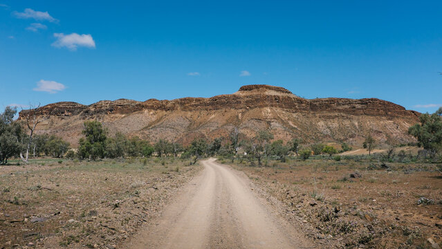 Gravel road leading towards imposing rock formation in the outback