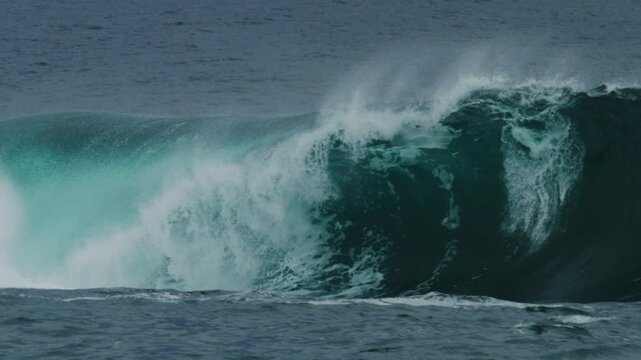 Telephoto close-up of rising wave wall as light passes through lip and spray shoots skyward