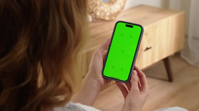 Woman use digital tech cell phone with green screen mock up. Hand tap press phone web site, open app. Girl hold mobile closeup. Turn on page. Cozy home background. Click online game copy space.