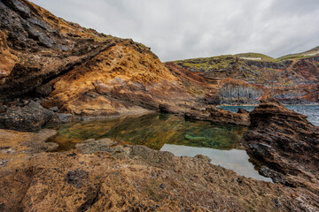 Dramatic geological formations along a rugged coastline with ocean views, showing volcanic layers, erosion textures and natural detail.